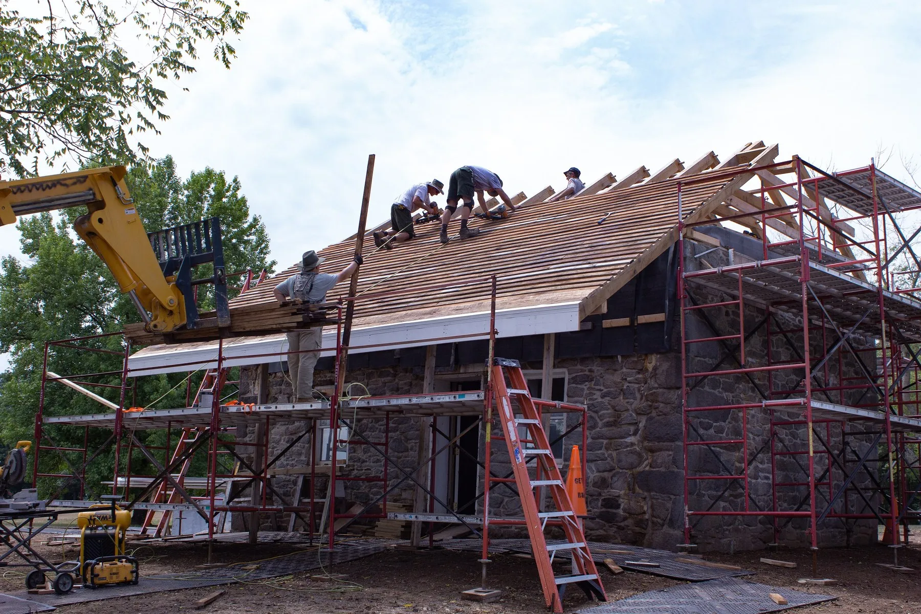 A roofing crew installing shingles on a steep residential roof from scaffolding