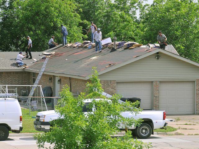 A roofing crew stripping and re-covering the roof of a single-storey house, work trucks parked in the driveway