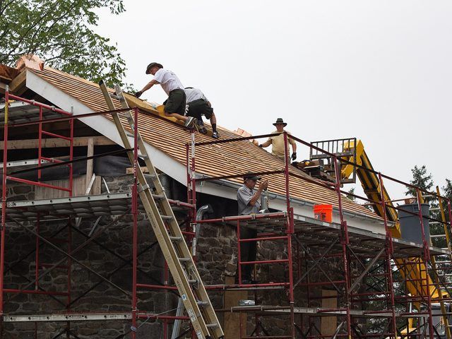 Workers on staging fitting decking boards up the slope of a roof