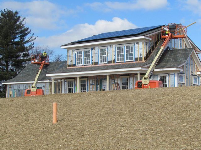 Two lifts raised against a large house while a crew works along the roof line