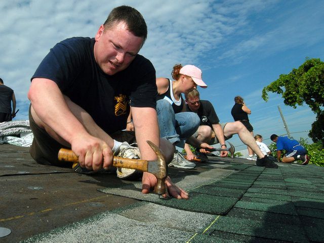 Close view of a worker nailing a course of shingles flat to a roof deck