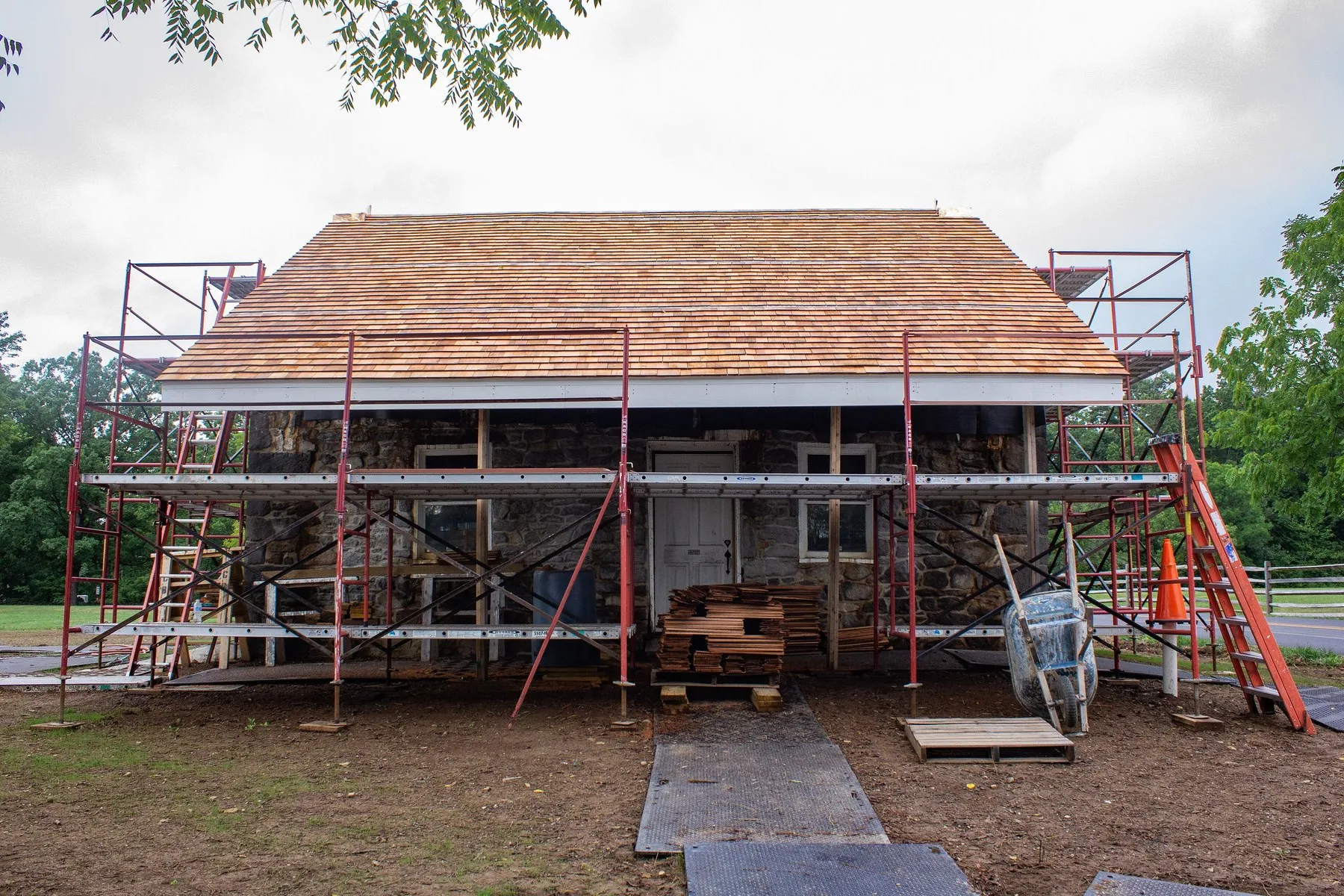 A stone house mid-restoration with new cedar shingles and scaffolding in place
